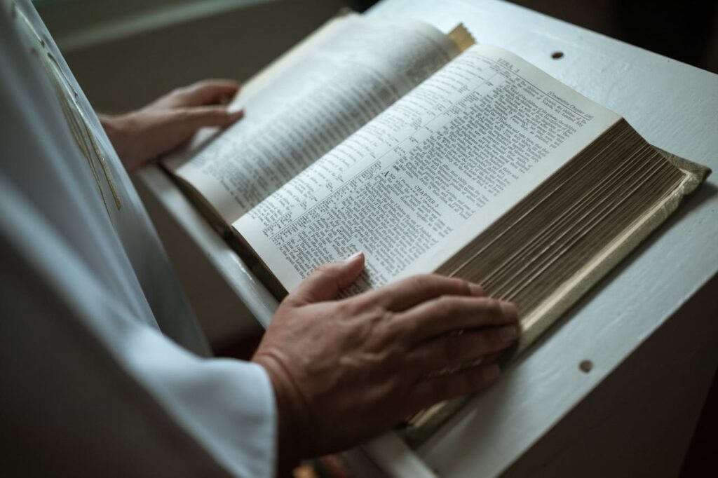 pexels-photo-5875444 A person in white garment holds an open religious scripture, focusing on hands and text.