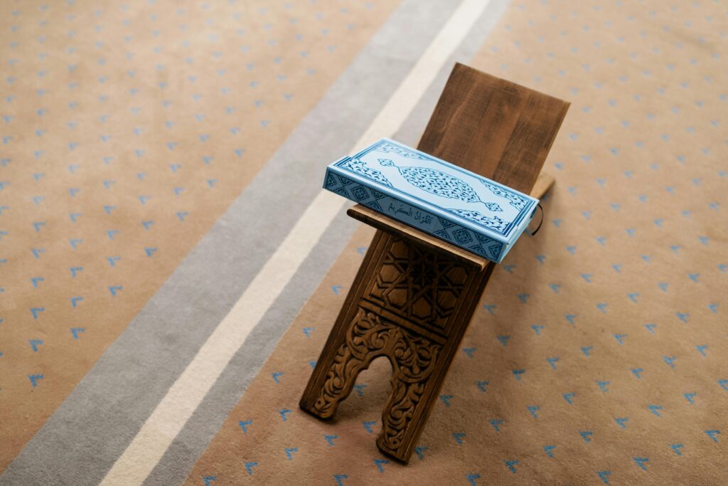 A Quran placed on an intricately carved wooden stand in a mosque setting.